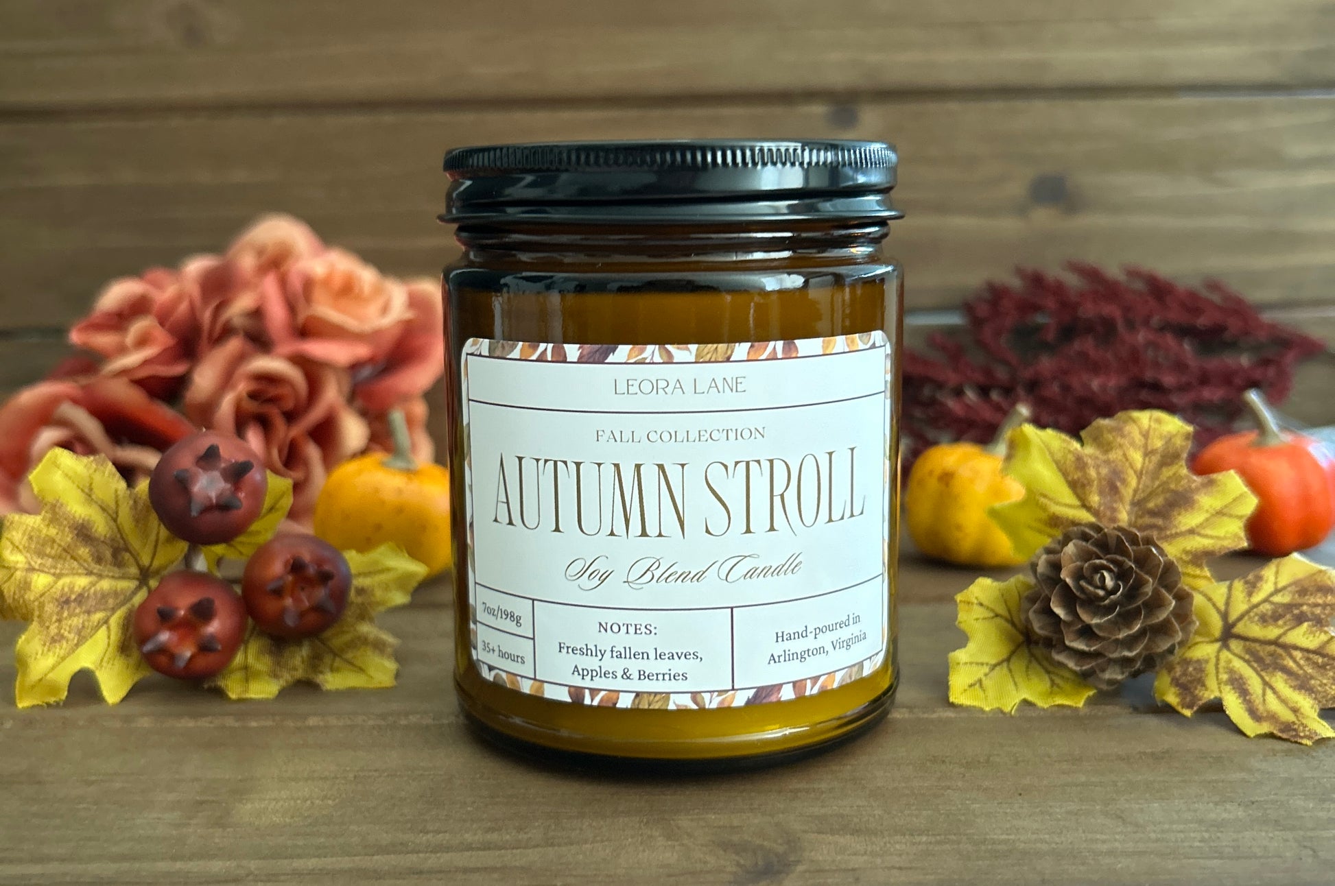 Candle labeled 'Autumn Stroll' with autumn decorations on a wooden background