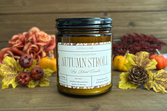 Candle labeled 'Autumn Stroll' with autumn decorations on a wooden background