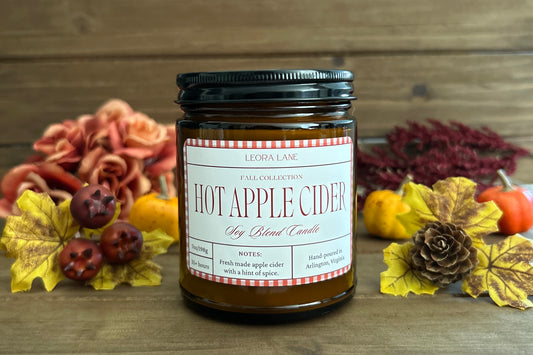 Candle labeled 'Hot Apple Cider' with autumn decorations on a wooden background