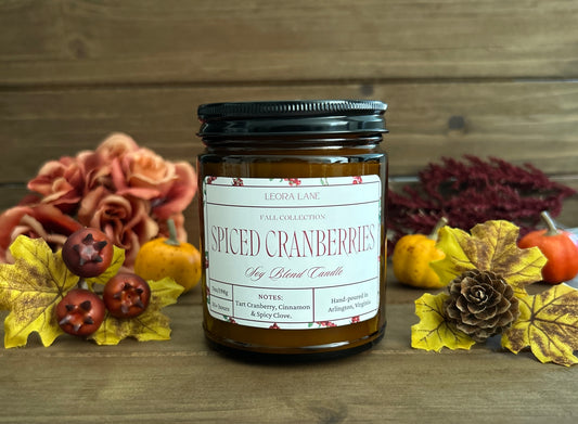 Candle jar labeled 'Spiced Cranberries' with autumn decorations on a wooden surface