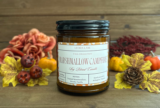 Candle labeled 'Marshmallow Campfire' with autumn decorations on a wooden background