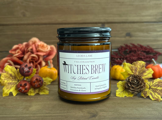 Candle jar labeled 'Witches Brew' with autumn decorations on a wooden surface